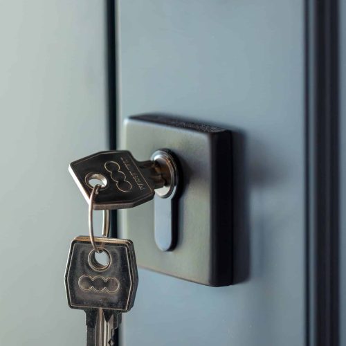 Vertical shot with keys in the lock of a blue door and a graphite handle. Cool palette, soft highlights and crisp geometry for a stylish interior.
